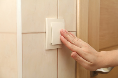 Photo of Woman pressing light switch indoors, closeup of hand