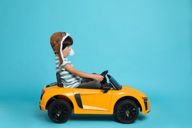 Photo of Cute little boy in pilot hat driving children's electric toy car on light blue background