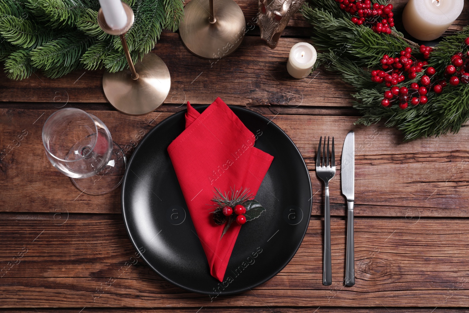 Photo of Plate with red fabric napkin, glass, cutlery and festive decor on wooden table, flat lay