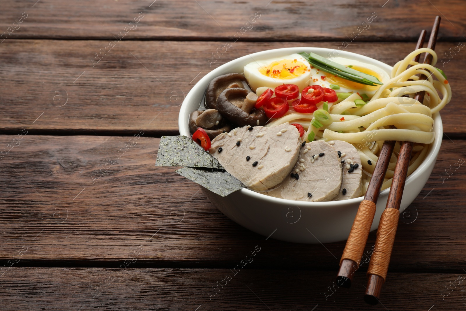 Photo of Delicious ramen with meat in bowl and chopsticks on wooden table, space for text. Noodle soup