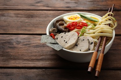 Delicious ramen with meat in bowl and chopsticks on wooden table, space for text. Noodle soup