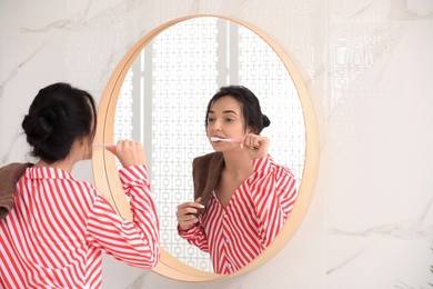 Young woman brushing teeth near mirror in bathroom