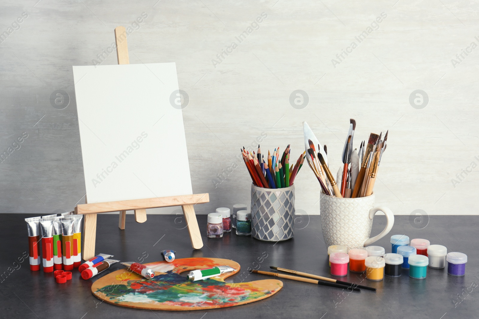 Photo of Easel with various artist tools on table against light wall. Space for text