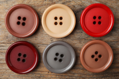 Many plastic sewing buttons on wooden background, flat lay