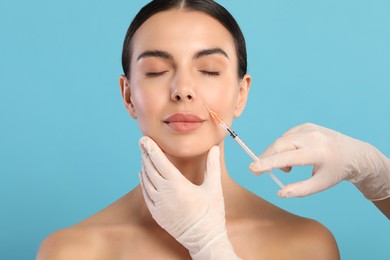 Photo of Doctor giving facial injection to young woman on light blue background. Cosmetic surgery
