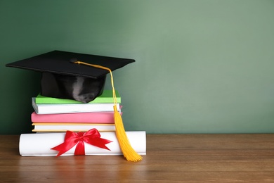 Photo of Graduation hat with books and diploma on table near chalkboard. Space for text