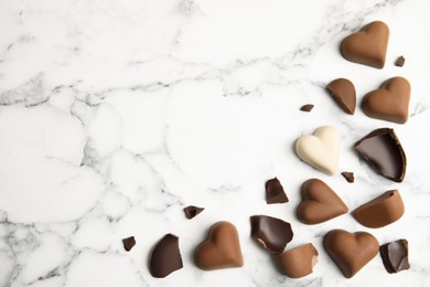 Tasty heart shaped chocolate candies on white marble table, flat lay with space for text. Happy Valentine's day
