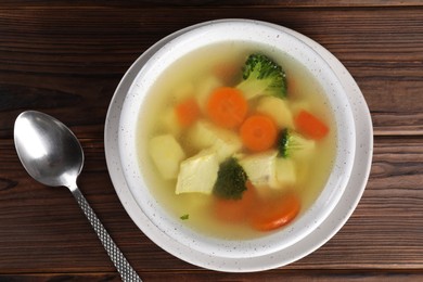 Photo of Tasty chicken soup with vegetables in bowl served on wooden table, top view