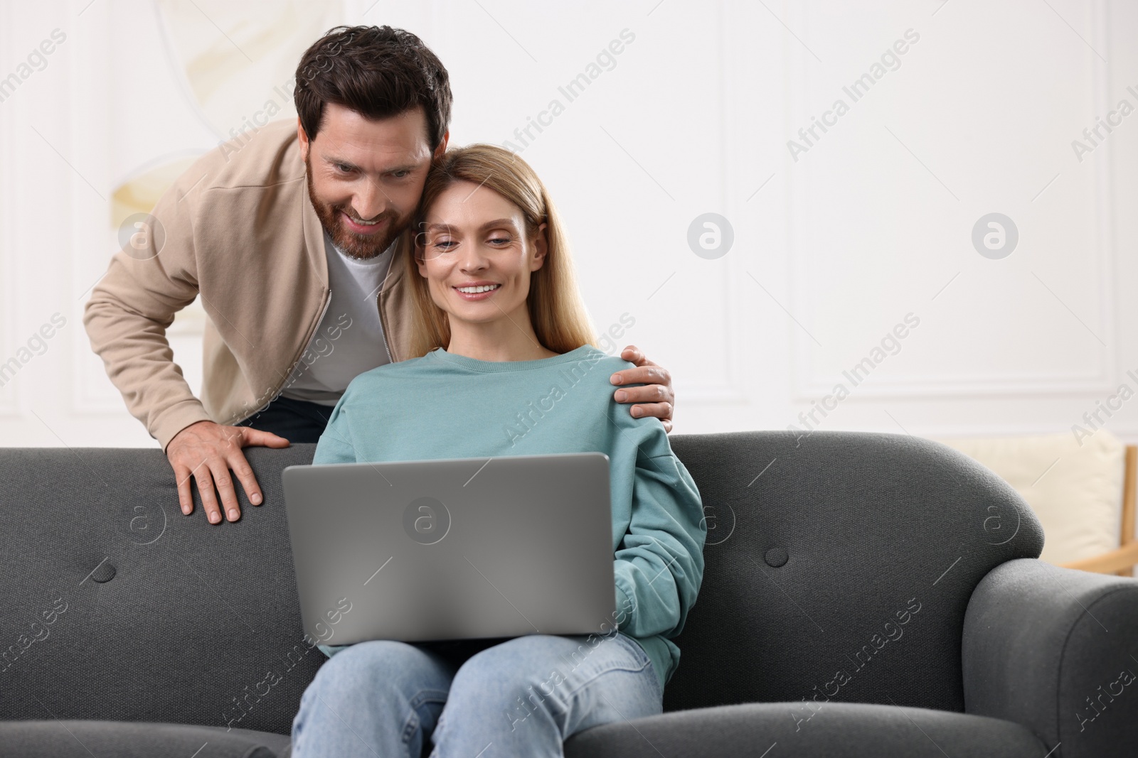 Photo of Happy couple with laptop on sofa at home. Space for text