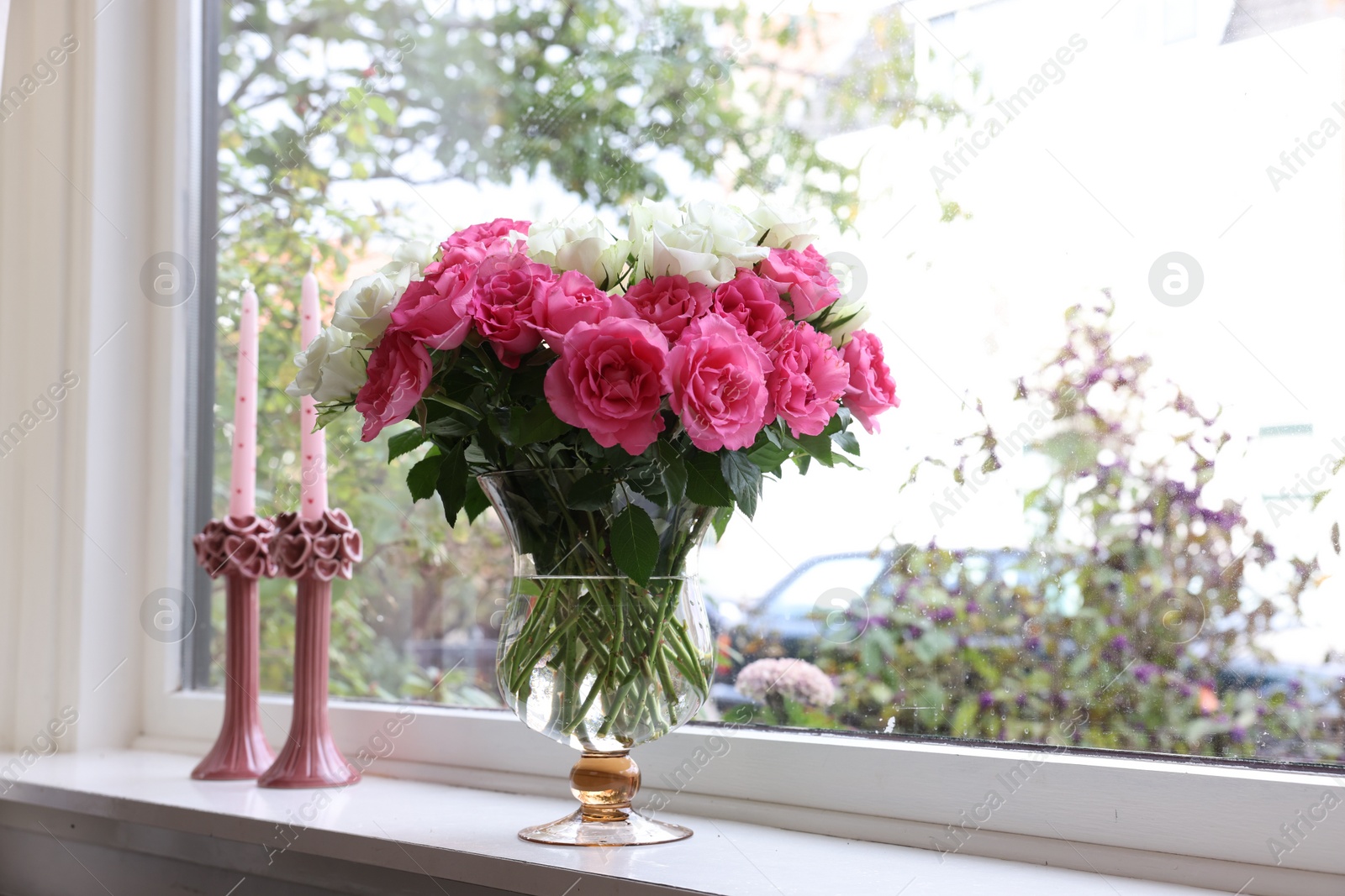 Photo of Vase with beautiful bouquet of roses and candles on windowsill indoors