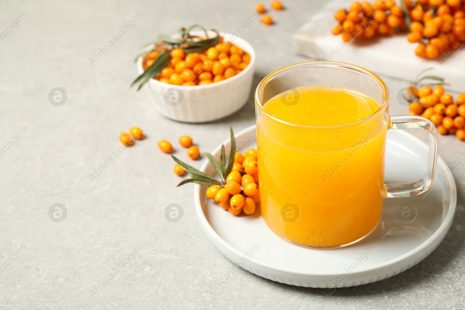 Photo of Delicious sea buckthorn tea and fresh berries on light grey table. Space for text