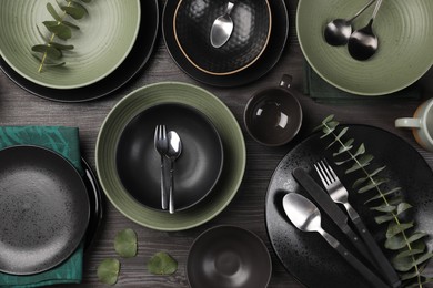 Stylish table setting with cutlery and eucalyptus branches on dark wooden background, flat lay