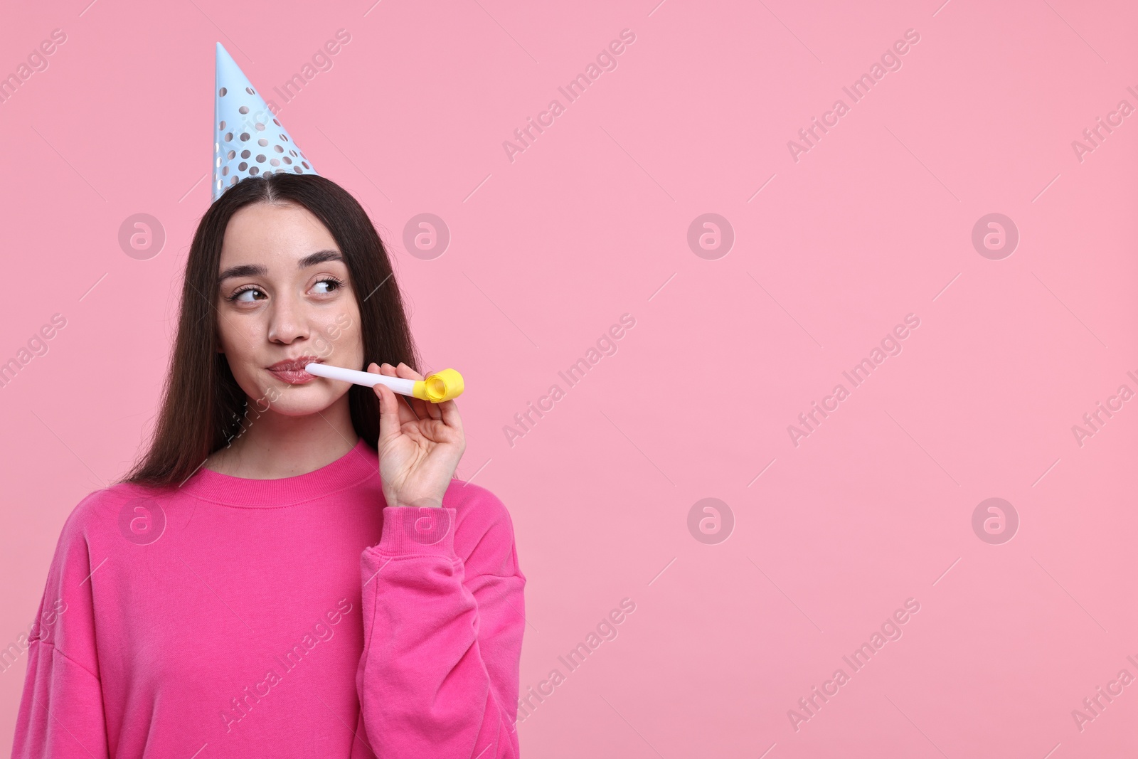 Photo of Woman in party hat with blower on pink background, space for text