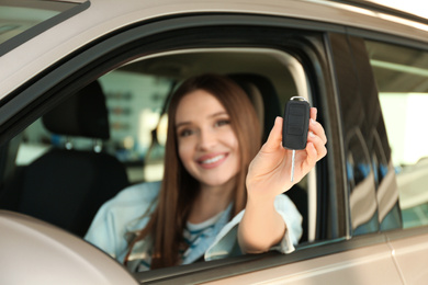 Photo of Beautiful woman sitting in modern car at dealership, focus on hand with key