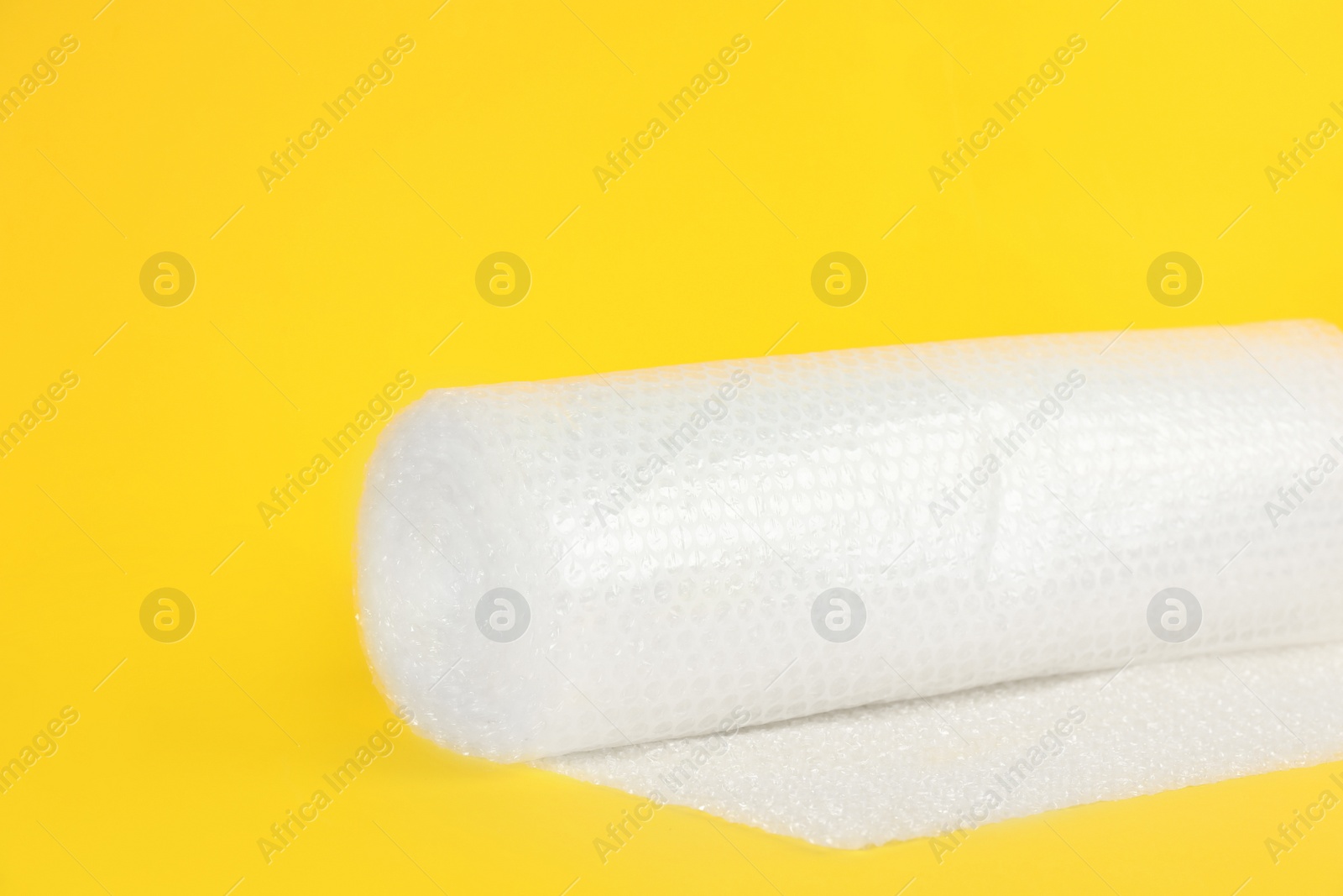 Photo of Bubble wrap roll on yellow background, space for text