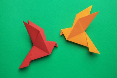 Photo of Beautiful colorful origami birds on green background, flat lay