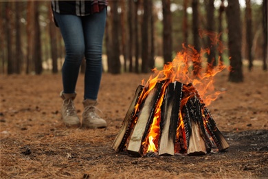 Photo of Woman near burning firewood in forest, closeup