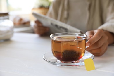 Photo of Woman holding glass cup with tea bag at white wooden table, closeup. Space for text