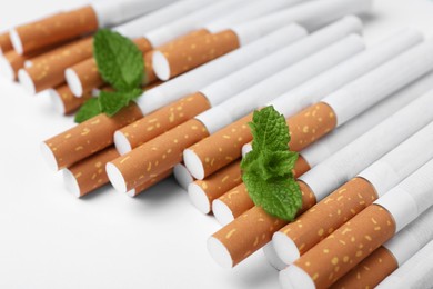 Menthol cigarettes and fresh mint leaves on white background, closeup