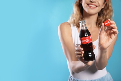 Photo of MYKOLAIV, UKRAINE - NOVEMBER 28, 2018: Young woman with bottle of Coca-Cola and cap on color background, closeup. Space for text