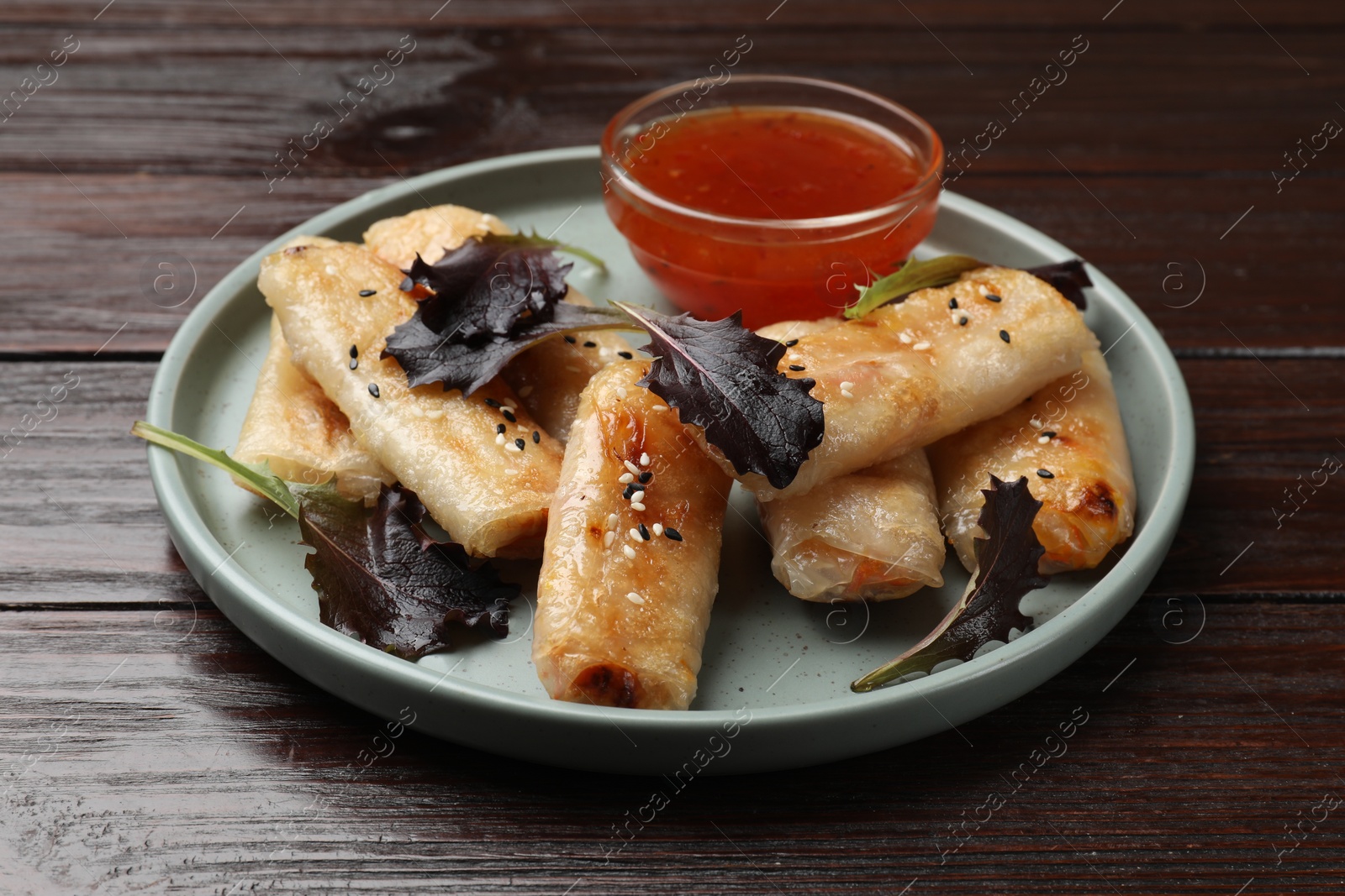 Photo of Tasty fried spring rolls, lettuce and sauce on wooden table