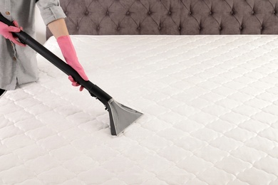 Woman disinfecting mattress with vacuum cleaner, closeup. Space for text