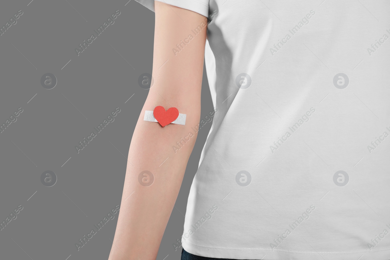 Photo of Blood donation concept. Woman with adhesive plaster on arm against grey background, closeup. Space for text