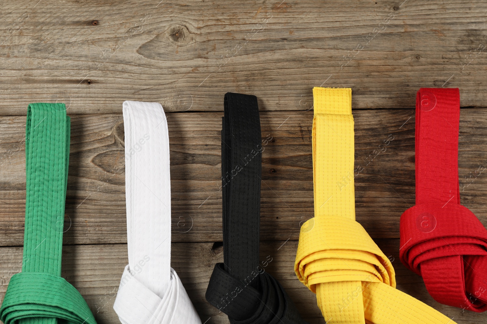 Photo of Colorful karate belts on wooden background, flat lay