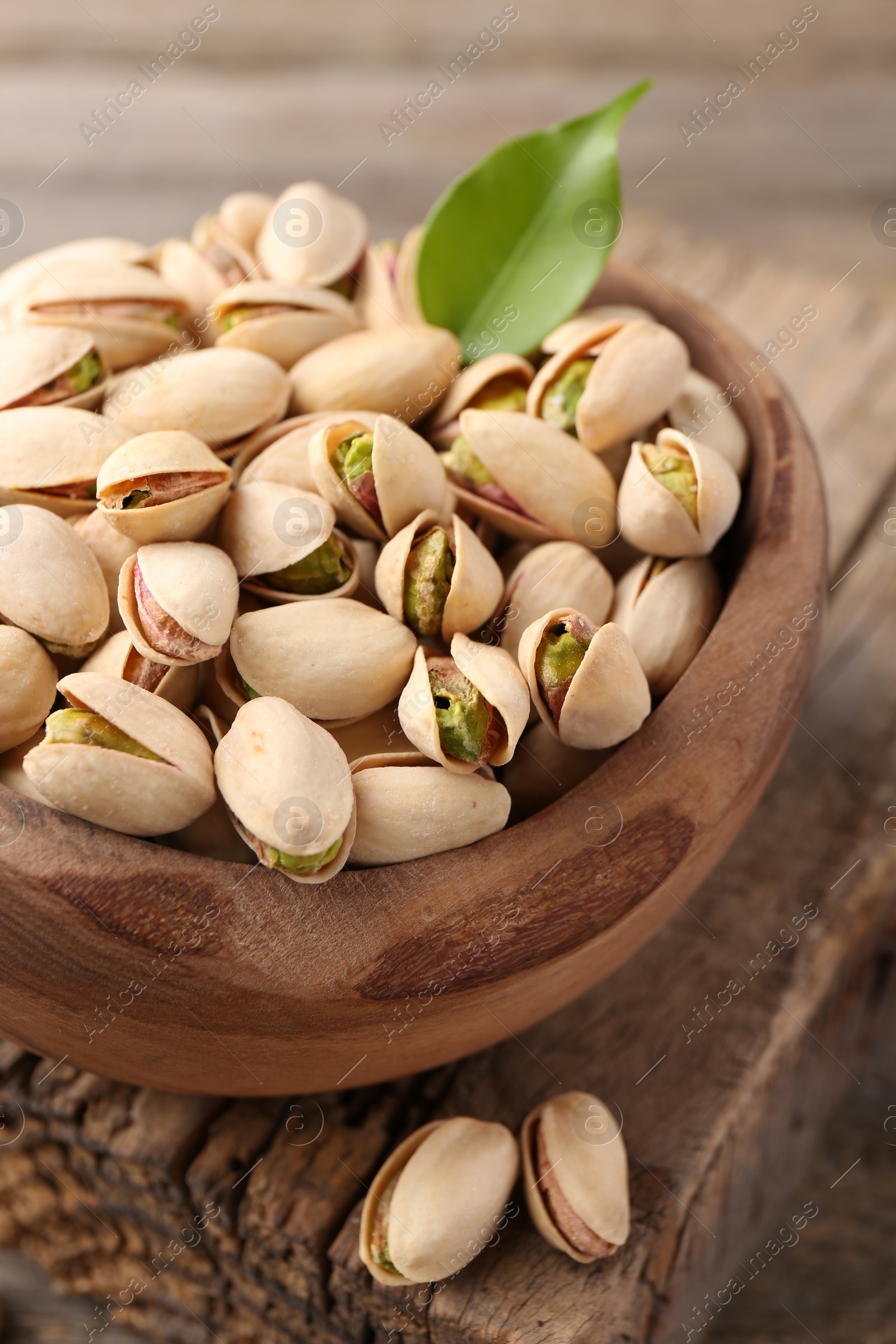 Photo of Delicious pistachios in bowl on wooden table, closeup