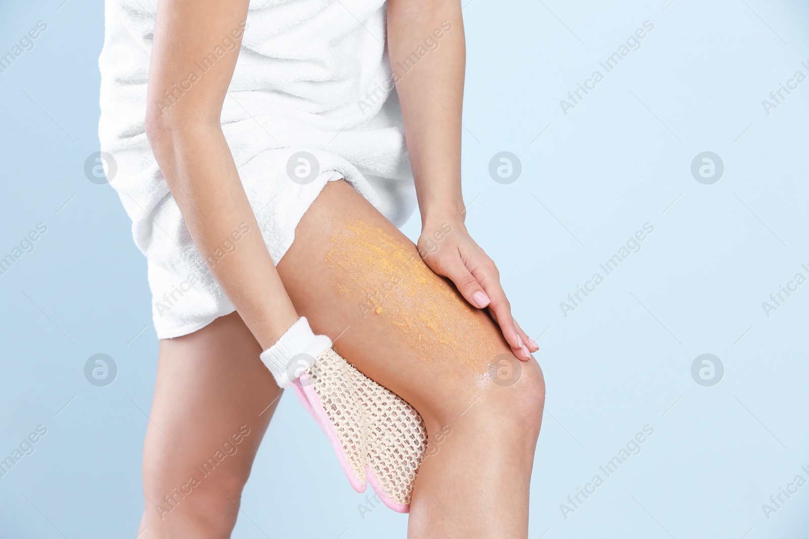 Photo of Young woman applying body scrub on leg against light background