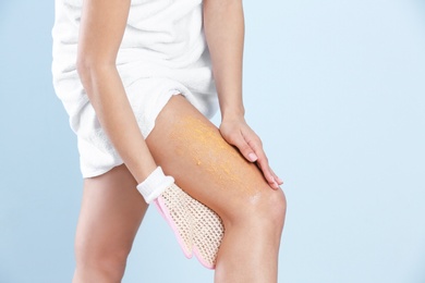 Young woman applying body scrub on leg against light background