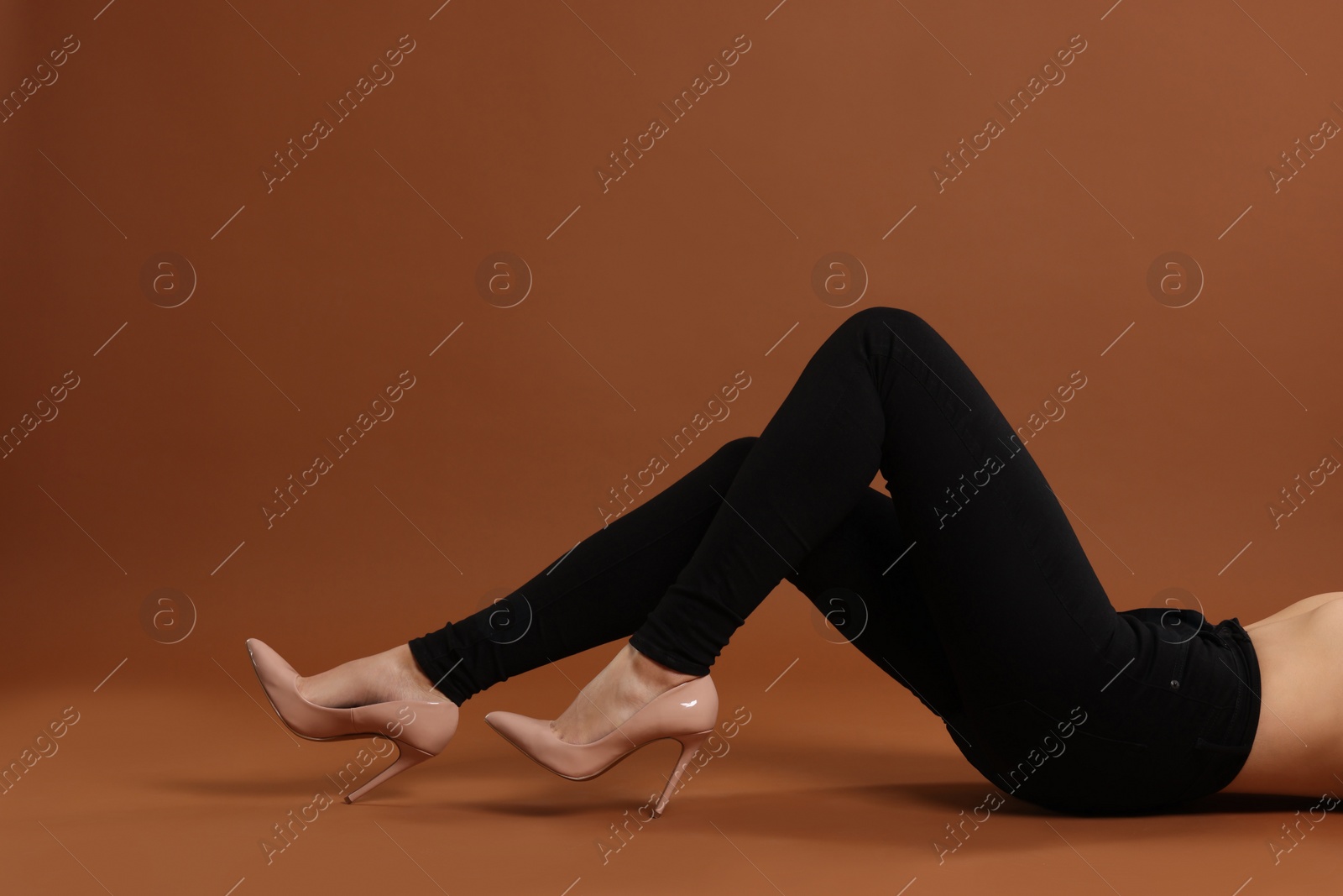 Photo of Woman wearing stylish black jeans and high heels shoes on brown background, closeup