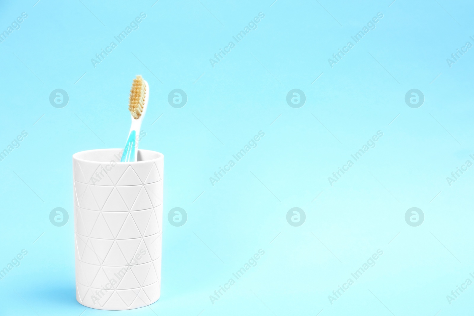 Photo of Natural bristle toothbrush in holder on light blue background. Space for text