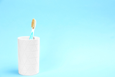 Photo of Natural bristle toothbrush in holder on light blue background. Space for text