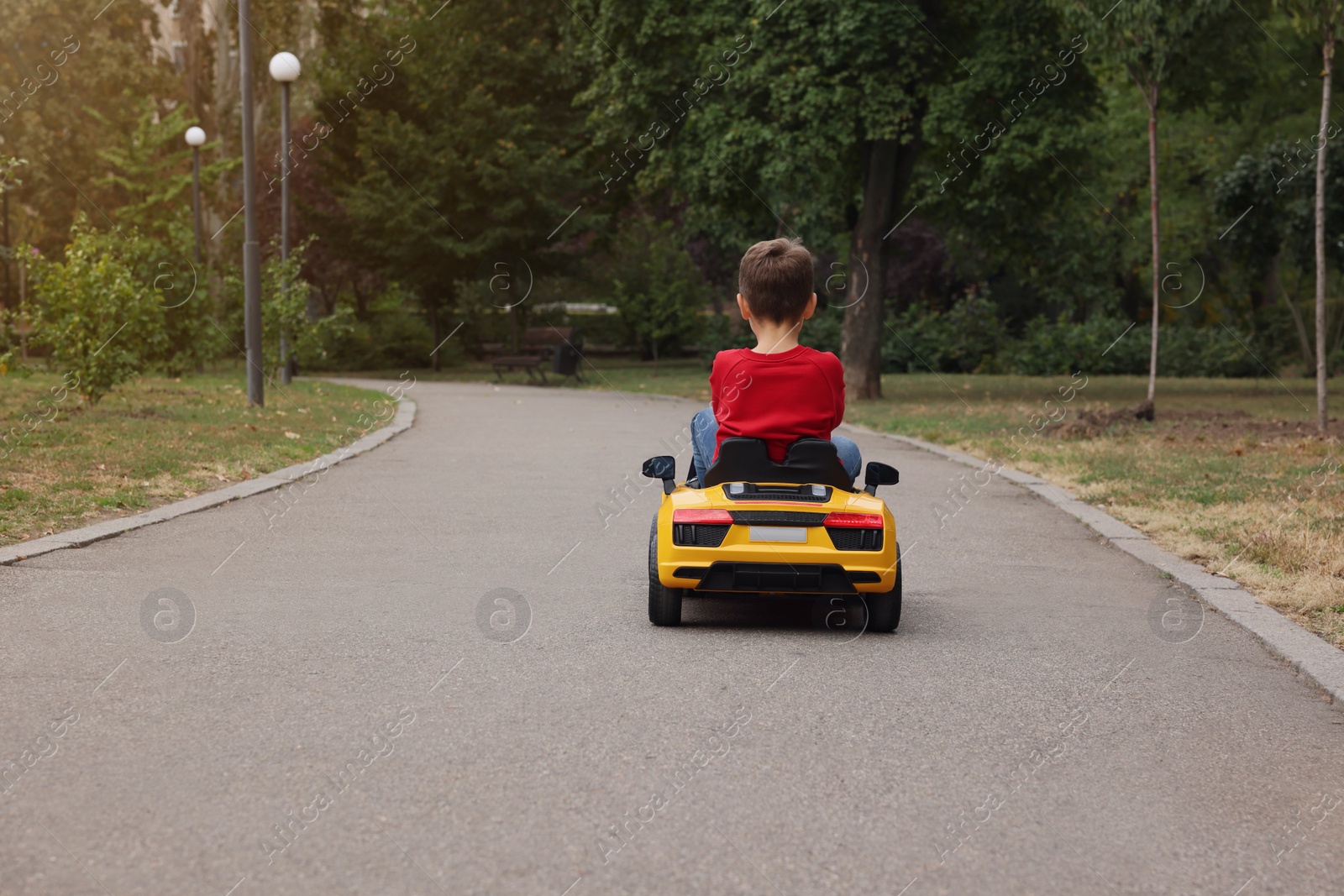 Photo of Cute little boy driving children's car outdoors, back view. Space for text