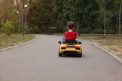 Photo of Cute little boy driving children's car outdoors, back view. Space for text