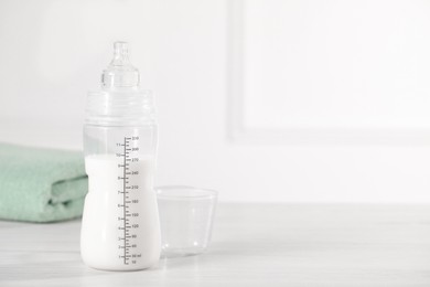 Feeding bottle with milk on white wooden table. Space for text