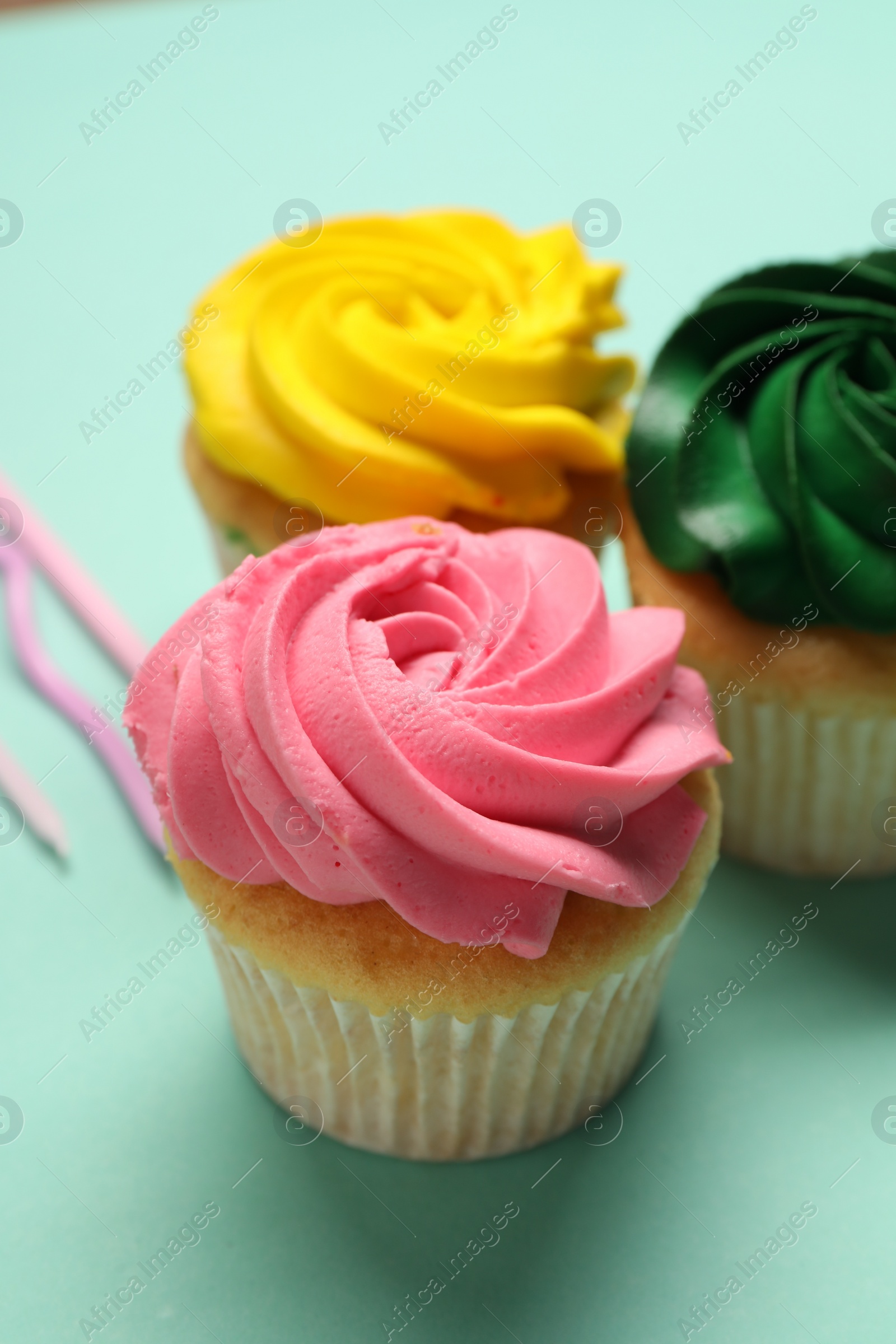 Photo of Delicious cupcakes with bright cream on turquoise background, closeup