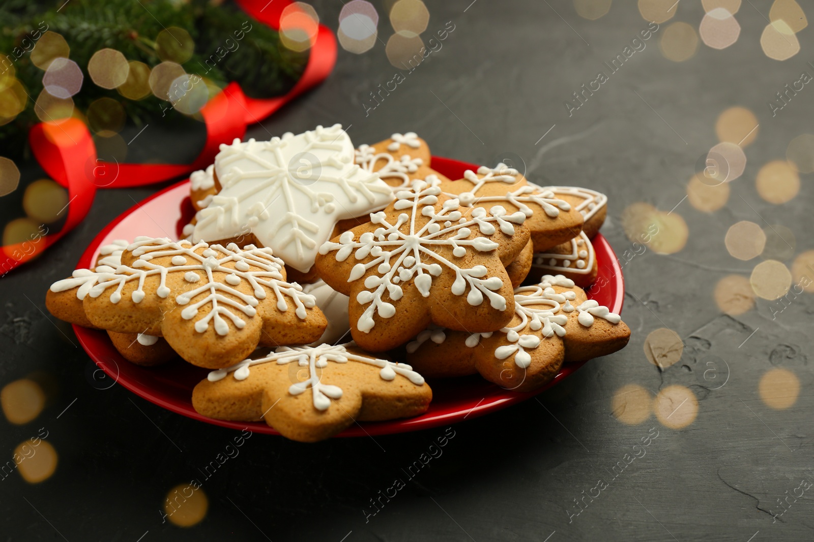 Photo of Tasty Christmas cookies with icing, fir branches and ribbon on black table. Space for text