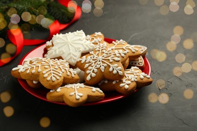 Tasty Christmas cookies with icing, fir branches and ribbon on black table. Space for text