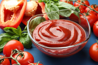 Photo of Bowl of tasty ketchup and ingredients on blue wooden table, closeup