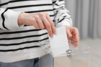 Photo of Woman putting her vote into ballot box on blurred background, closeup