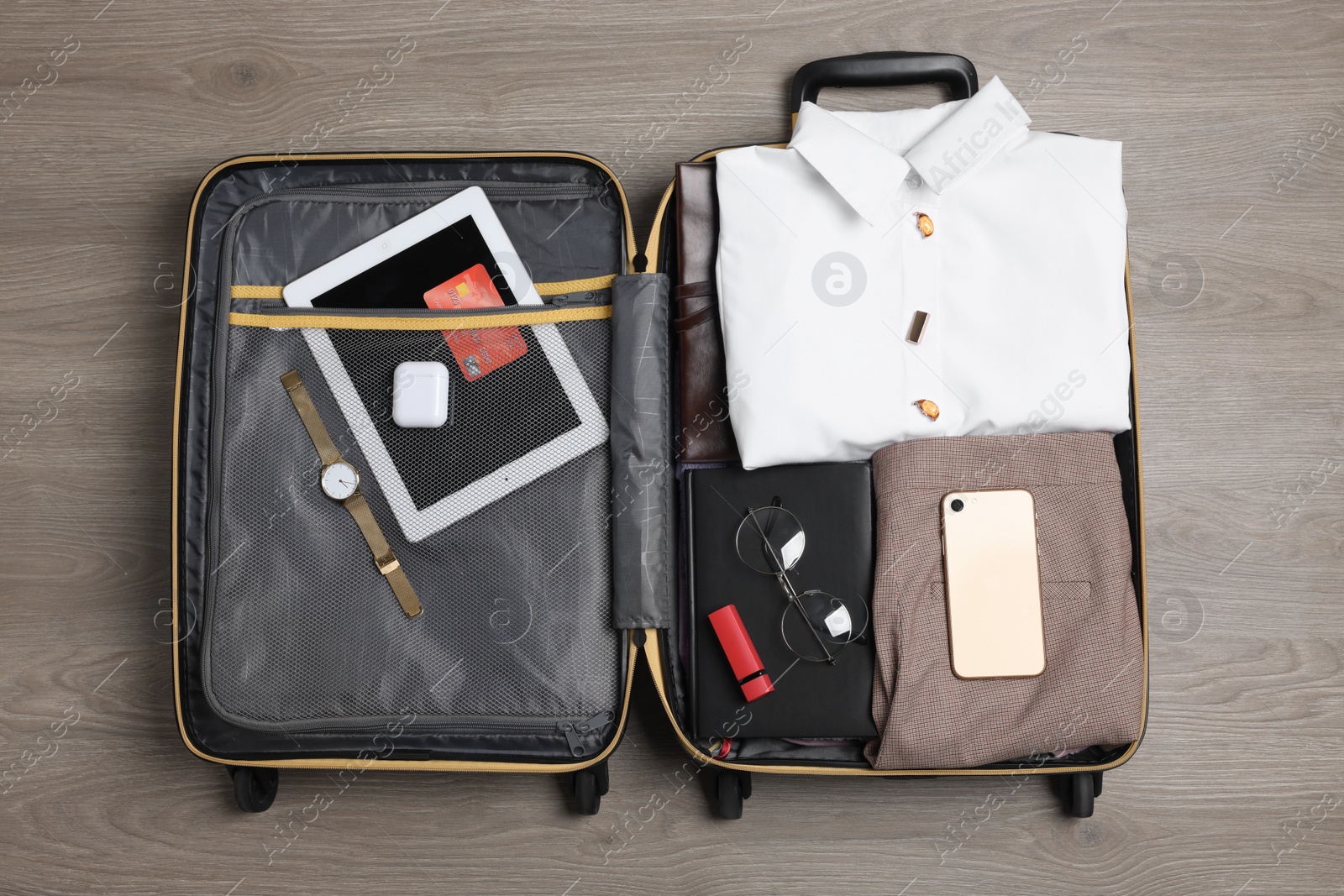 Photo of Folded clothes and accessories in open suitcase on wooden background, top view. Packing for business trip