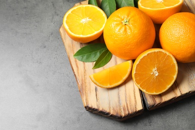 Photo of Wooden board with ripe oranges on grey background. Space for text