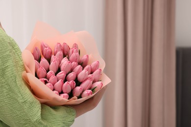 Photo of Woman holding bouquet of pink tulips indoors, closeup. Space for text