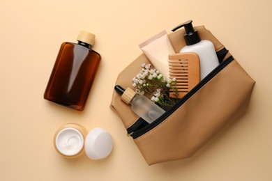 Photo of Preparation for spa. Compact toiletry bag with different cosmetic products and flowers on beige background, flat lay