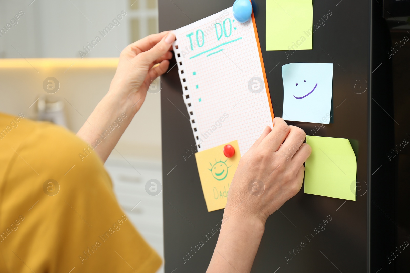 Photo of Woman putting blank to do list on refrigerator door in kitchen, closeup