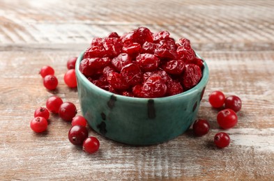 Photo of Tasty dried cranberries in bowl and fresh ones on rustic wooden table, closeup