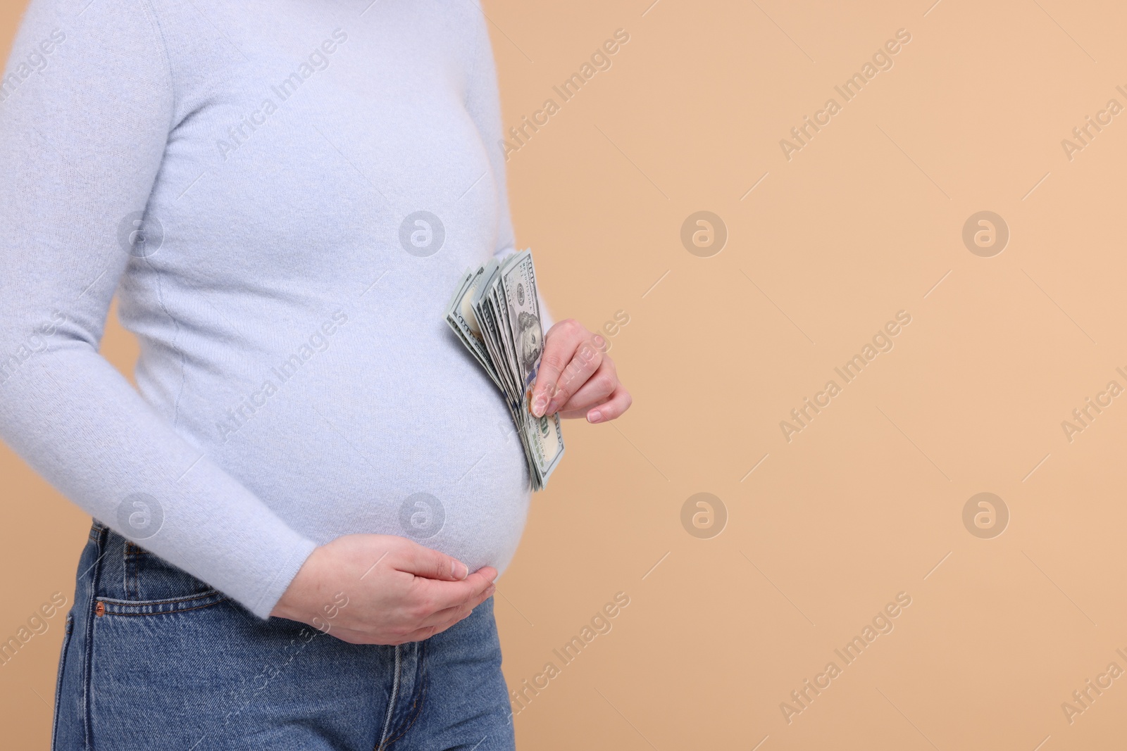 Photo of Surrogate mother. Pregnant woman with dollar banknotes on beige background, closeup. Space for text