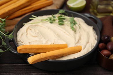 Photo of Delicious hummus with grissini sticks and ingredients on wooden table, closeup